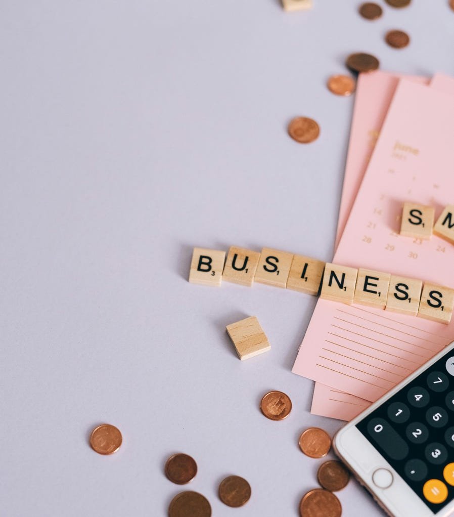 Flat lay of a small business planning scene with coins, smartphone calculator, and letter tiles.